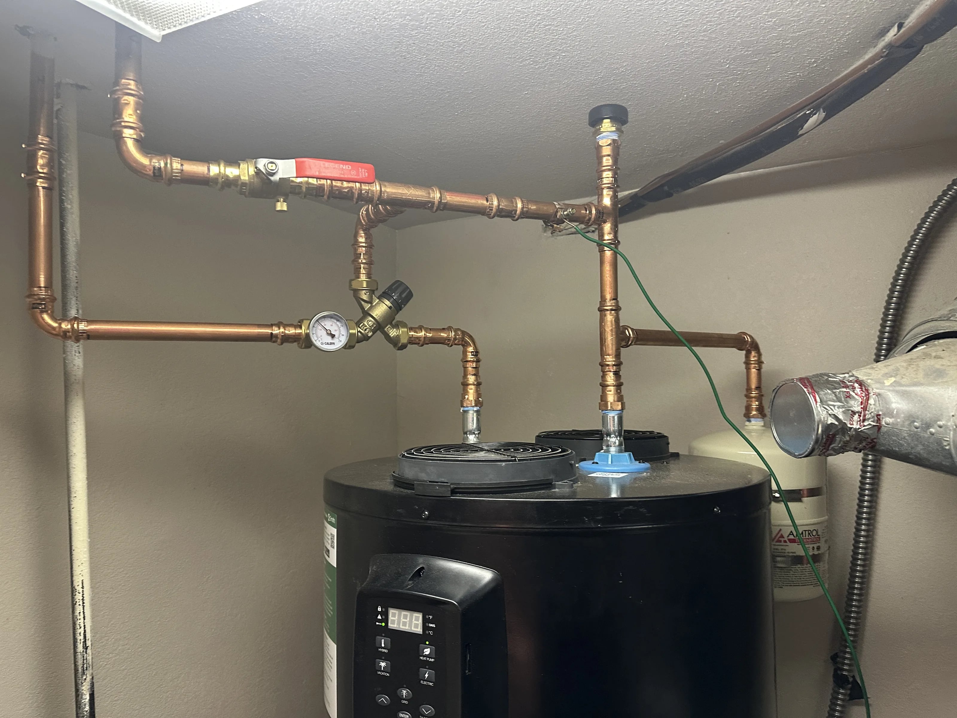 New copper piping with a mixing valve and expansion tank above a heat pump water heater.
